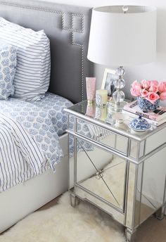 a bedroom with a mirrored nightstand and pink flowers on the side table next to it