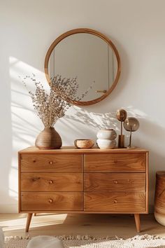 a wooden dresser sitting next to a round mirror on top of a white wall in a room