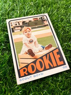 a baseball card laying in the grass with a baby on it