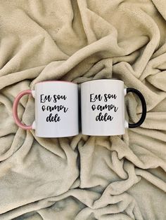 two coffee mugs sitting on top of a bed next to a white and pink blanket