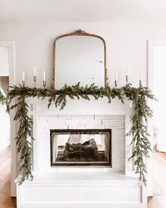 a white fireplace decorated with greenery and candles