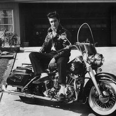 a man sitting on top of a motorcycle parked in front of a garage with his feet propped up