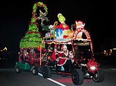 people in santa costumes riding on a cart decorated with christmas lights and decorations at night