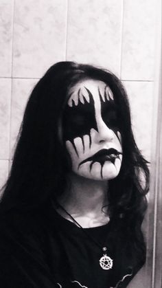 a woman with makeup painted on her face and black hair is standing in front of a tiled wall