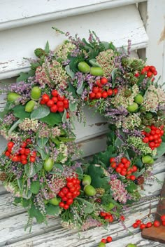 a wreath with red berries and green leaves on a white door frame next to an old wooden bench