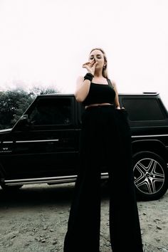 a woman standing in front of a black truck talking on a cell phone while wearing wide legged pants