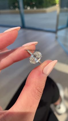 a woman's hand holding an engagement ring in front of her face, with the diamond