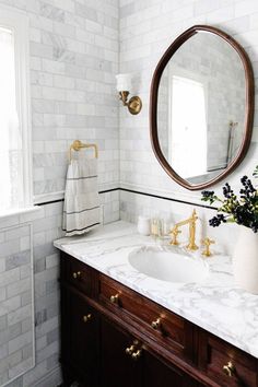 a bathroom with marble counter tops and gold faucets on the vanity, along with a round mirror