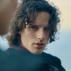 a close up of a person with curly hair and a black shirt looking at the camera