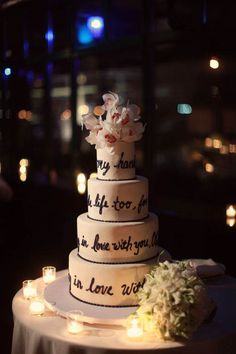 a wedding cake sitting on top of a table with lit candles around it and flowers