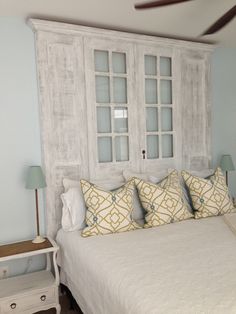 a bed with white linens and pillows in front of an old wooden headboard