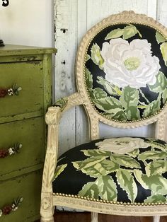 an old chair with flowers painted on it in front of a green dresser and chest of drawers