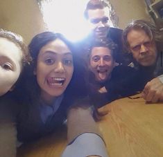 a group of people standing around a wooden table with their faces on the table and one person sticking his tongue out