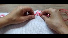 two hands are working on an ornament with red and white ribbon around it