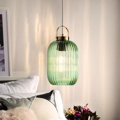 a green glass light hanging over a bed next to a vase with flowers on it