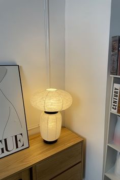 a white lamp sitting on top of a wooden table next to a book shelf filled with books