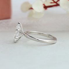 a white gold ring with a heart shaped diamond on the side, sitting next to a flower