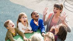 a group of children sitting on the ground with their hands in the air and laughing