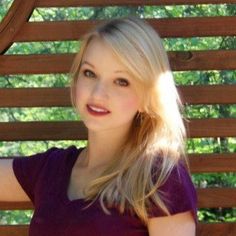 a woman sitting on a wooden bench with her arms crossed and looking at the camera