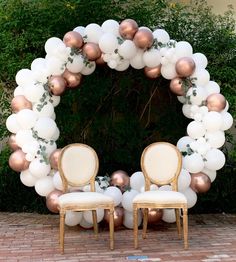 two chairs sitting in front of a white and rose gold balloon arch with greenery