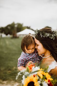 a woman holding a small child in her arms and wearing a flower crown on her head