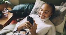 a woman sitting on a couch looking at her cell phone while listening to headphones