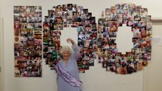 an older woman standing in front of a wall with pictures on it and holding her arms up