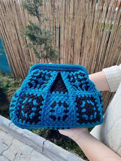 a person holding up a blue crocheted purse