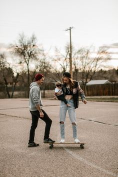 a man riding a skateboard next to a woman holding a baby on top of it