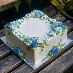 a white and blue square cake sitting on top of a wooden table next to flowers