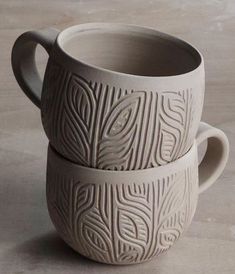 two white cups sitting next to each other on top of a wooden table with designs