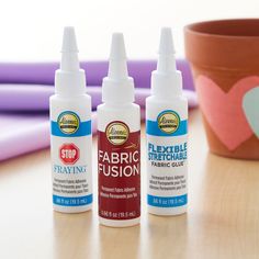 three bottles of fabric glue sitting next to a potted plant