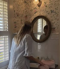 a woman standing in front of a bathroom mirror next to a sink under a light