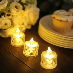 three lit candles sitting on top of a table next to cupcakes and flowers