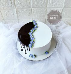 a white cake with blue flowers and drips on the top is sitting on a table