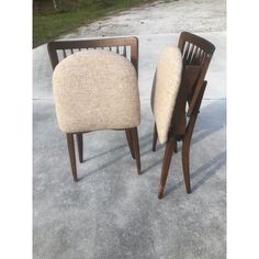 two wooden chairs sitting next to each other on top of a cement ground with grass in the background