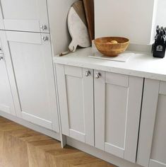 a wooden bowl sitting on top of a kitchen counter next to white cupboards and drawers