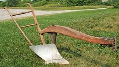 an old shovel leaning against a wooden sled on the grass in front of a road