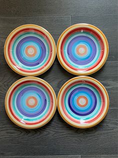 four multicolored plates sitting on top of a wooden table next to each other