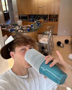 a young man is drinking from a blue cup in the middle of a kitchen area