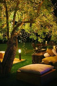 an outdoor seating area is lit up at night with lights on the trees and lawn furniture