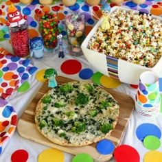 a table topped with a pizza covered in toppings next to a bowl of popcorn