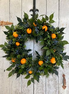 a wreath with oranges and blue berries hanging on a white wooden wall next to an iron hook