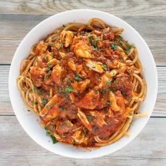 a white bowl filled with pasta covered in sauce and parmesan cheese on top of a wooden table