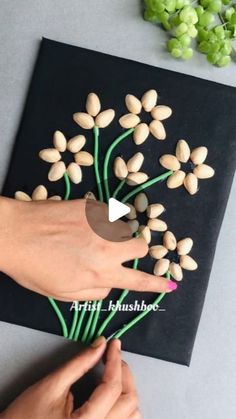 someone is making a flower arrangement out of almonds on a black paper with green stems