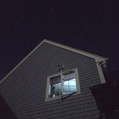 a window on the side of a gray house at night with stars in the sky