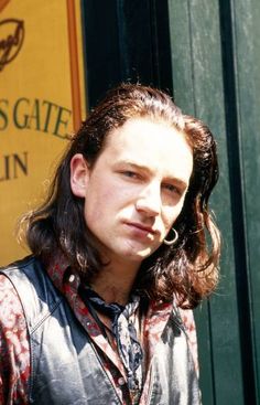 a man with long hair standing in front of a green door wearing a leather jacket