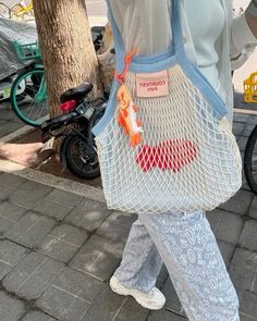 a woman walking down the street carrying a netted bag