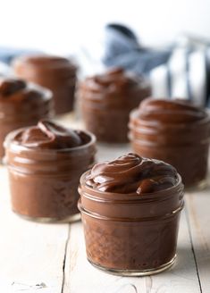 four jars filled with chocolate pudding on top of a wooden table