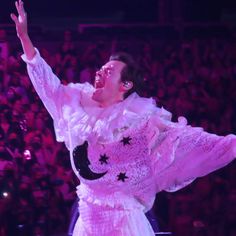 a woman in a white dress is on stage with her arms up and hands out